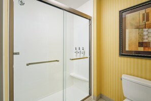 A bathroom with a glass shower enclosure, a toilet, and a wall-mounted sink with toiletries.