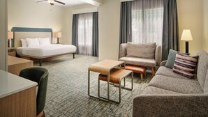 A hotel room with a bed, a desk, a chair, a sofa, a small table, and a ceiling fan.