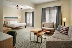 A hotel room with a bed, a desk, a chair, a sofa, a small table, and a ceiling fan.