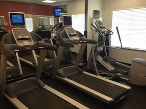 A gym with treadmills, stationary bikes, and a mirrored wall.
