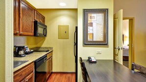 A compact kitchen with wooden cabinets, a microwave, and a coffee maker. There is a dining table with chairs and a framed artwork on the wall.