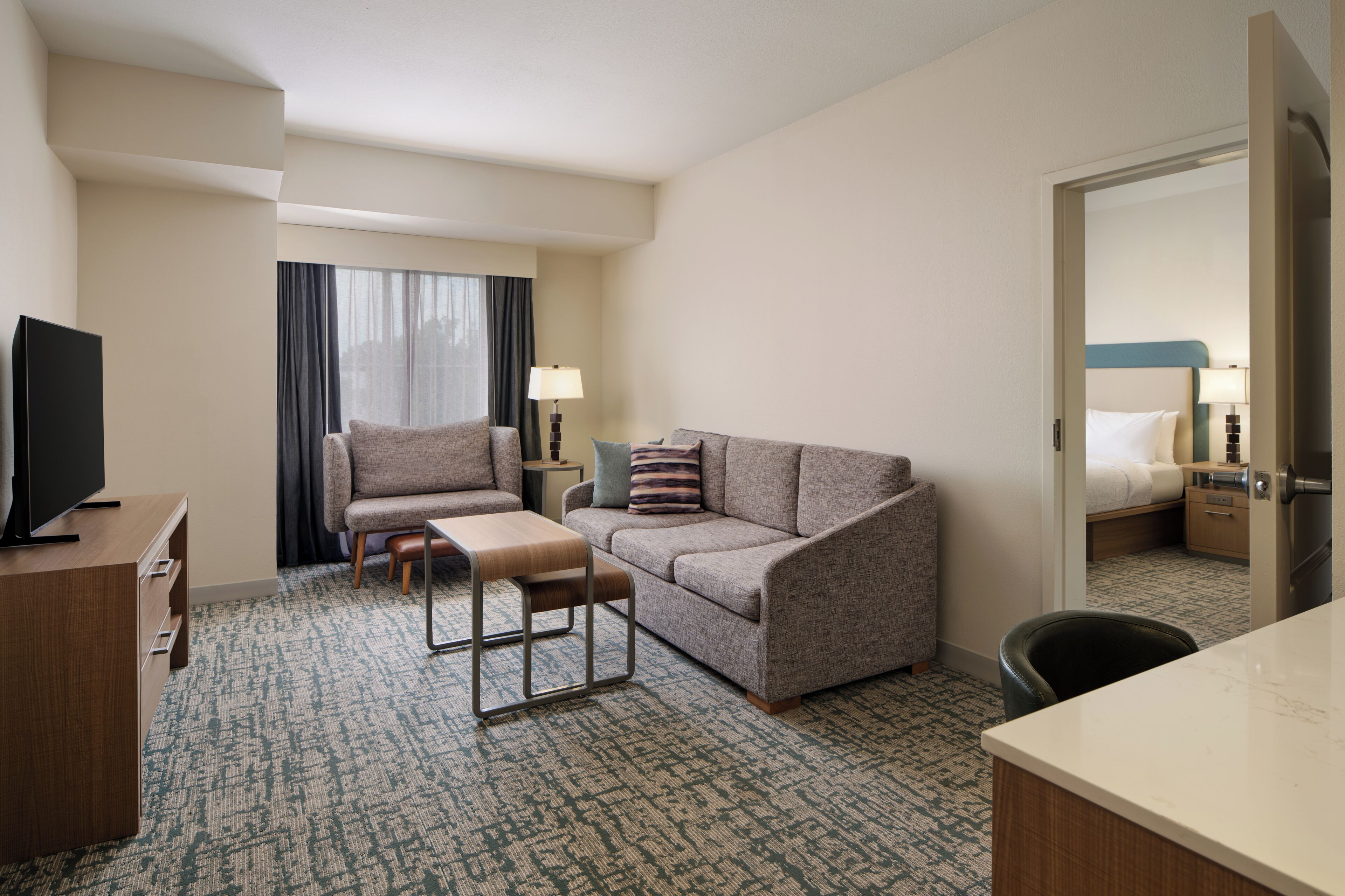 Una habitación de hotel con sofá, sillón, una mesita, televisor y cama.
