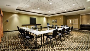 A conference room with tables and chairs, a projector screen, and a patterned carpet.