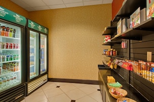 Una kitchenette de hotel con un refrigerador lleno de bebidas, un estante con condimentos y una encimera con aperitivos.