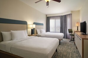 A hotel room with two beds, a desk, a television, and a ceiling fan.