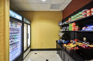 Interior de un supermercado con bebidas refrigeradas, pasillos de aperitivos y una pared con diseño.