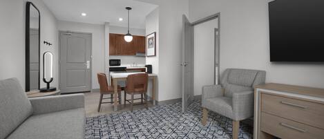 Una sala de estar moderna con un sofá y un sillón grises, y un aparador de madera. Hay un comedor con una mesa y sillas, y una cocina con armarios de madera y un microondas.