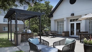 Un patio al aire libre con mobiliario de mimbre, una parrilla y una zona de estar cubierta.