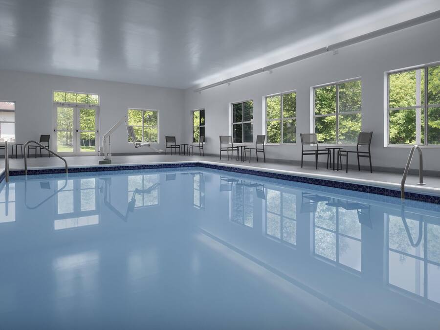 A large indoor swimming pool with clear glass walls, surrounded by windows offering views of greenery.