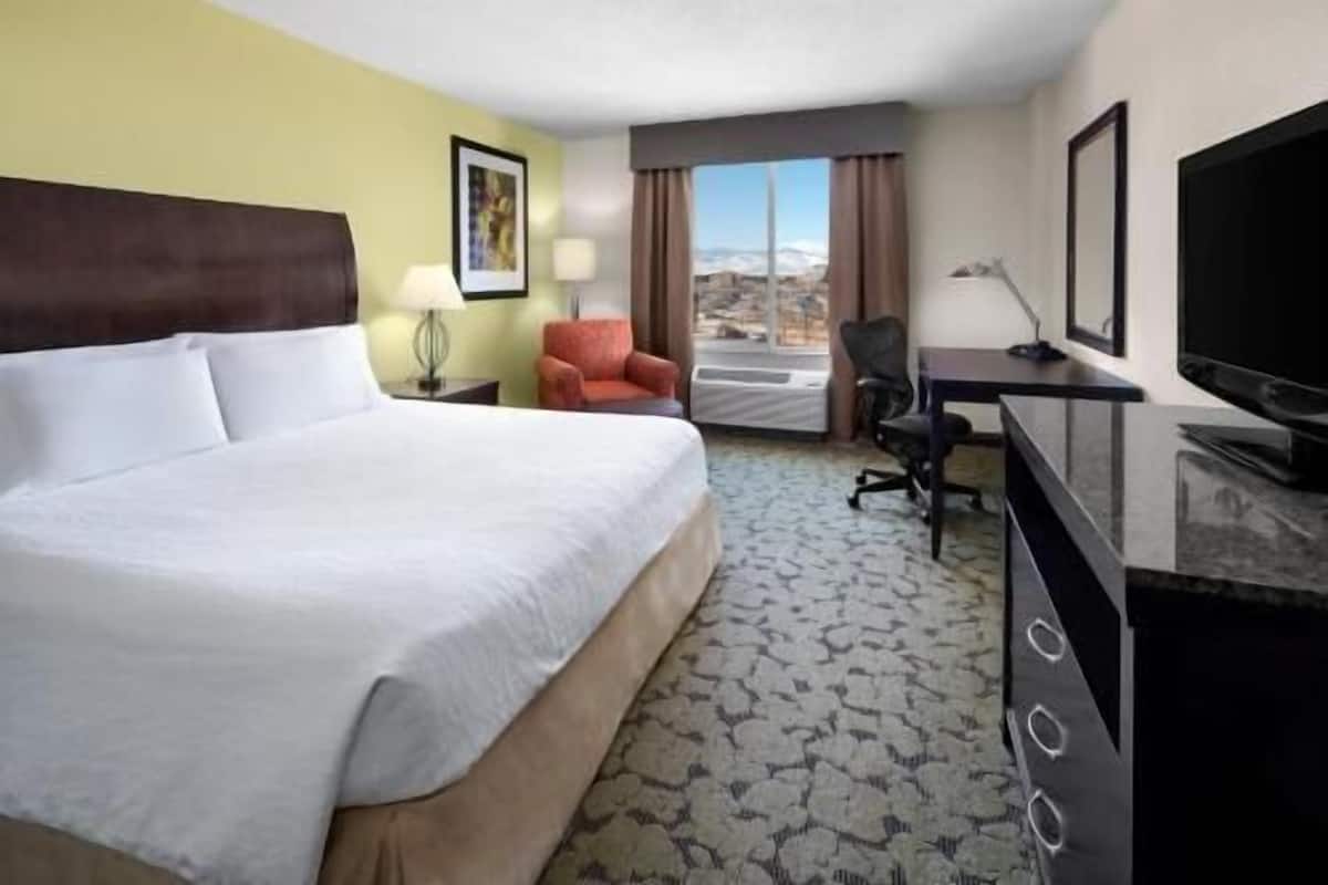 Habitación de hotel con cama, escritorio, silla, televisor y ventana con vistas.