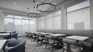 A modern dining area with multiple tables and chairs, large windows, and a patterned carpet. - Hilton Garden Inn Denver/Highlands Ranch (Littleton)