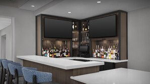 A modern bar area with a long counter, multiple seating options, and a large flat-screen TV mounted above the bar. - Hilton Garden Inn Denver/Highlands Ranch (Littleton)