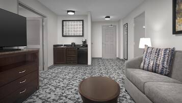 Camera d'albergo con televisore a schermo piatto, angolo cottura, divano con cuscini decorati e tavolino rotondo.