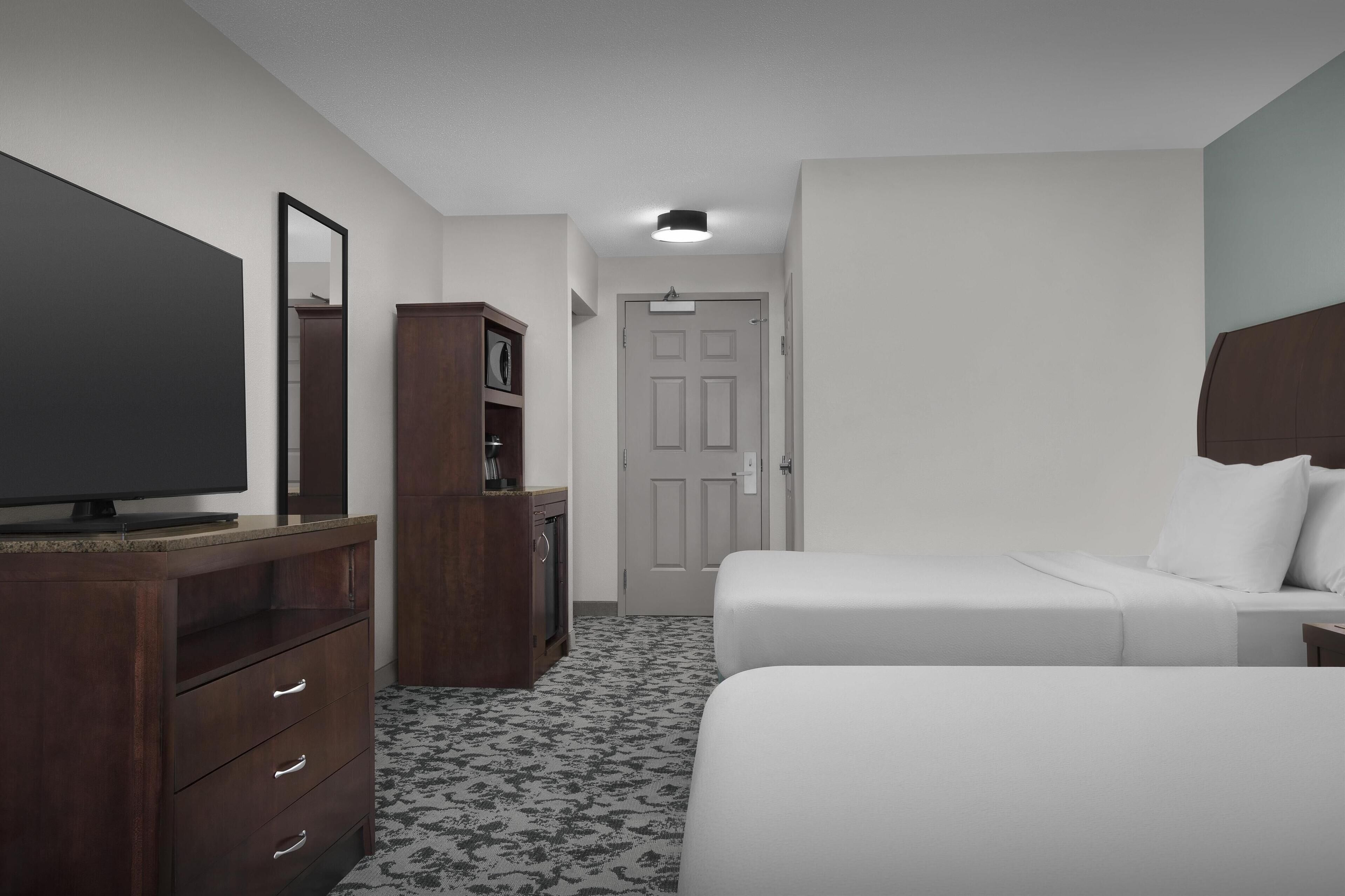 Una habitación de hotel con cama, televisor, cómoda y puerta.