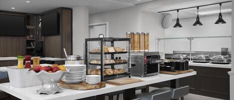 A modern kitchen with a central island, bar stools, a coffee station, and a glass-fronted pastry display.