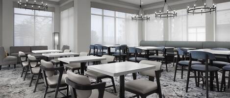 A modern dining area with tables and chairs, large windows, and chandeliers.