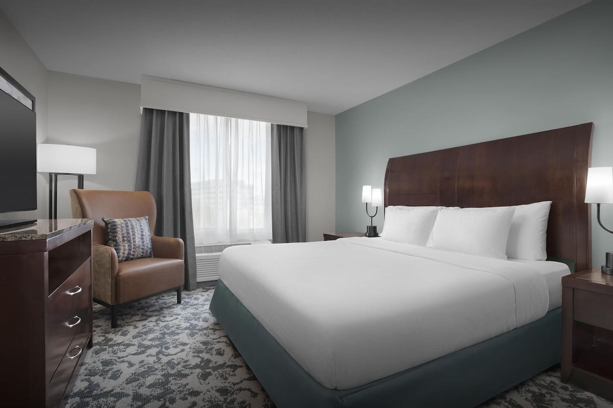 Una habitación de hotel con una cama grande, un escritorio con lámpara, una silla y un televisor.