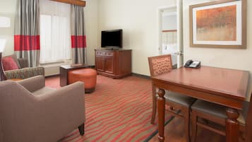 A hotel room with a dining table, two chairs, a television, a cabinet, and a bed in the background.