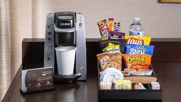 Máquina de café, bandeja de lanches e garrafa de água sobre um balcão de hotel.