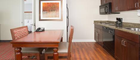 A hotel room with a wooden dining table, chairs, a microwave, a coffee maker, and a painting on the wall.