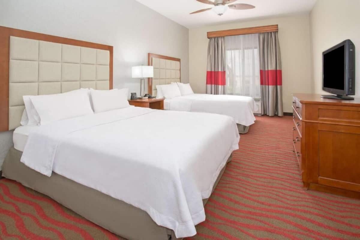 A hotel room with two beds, a television, a desk, and a window with curtains.