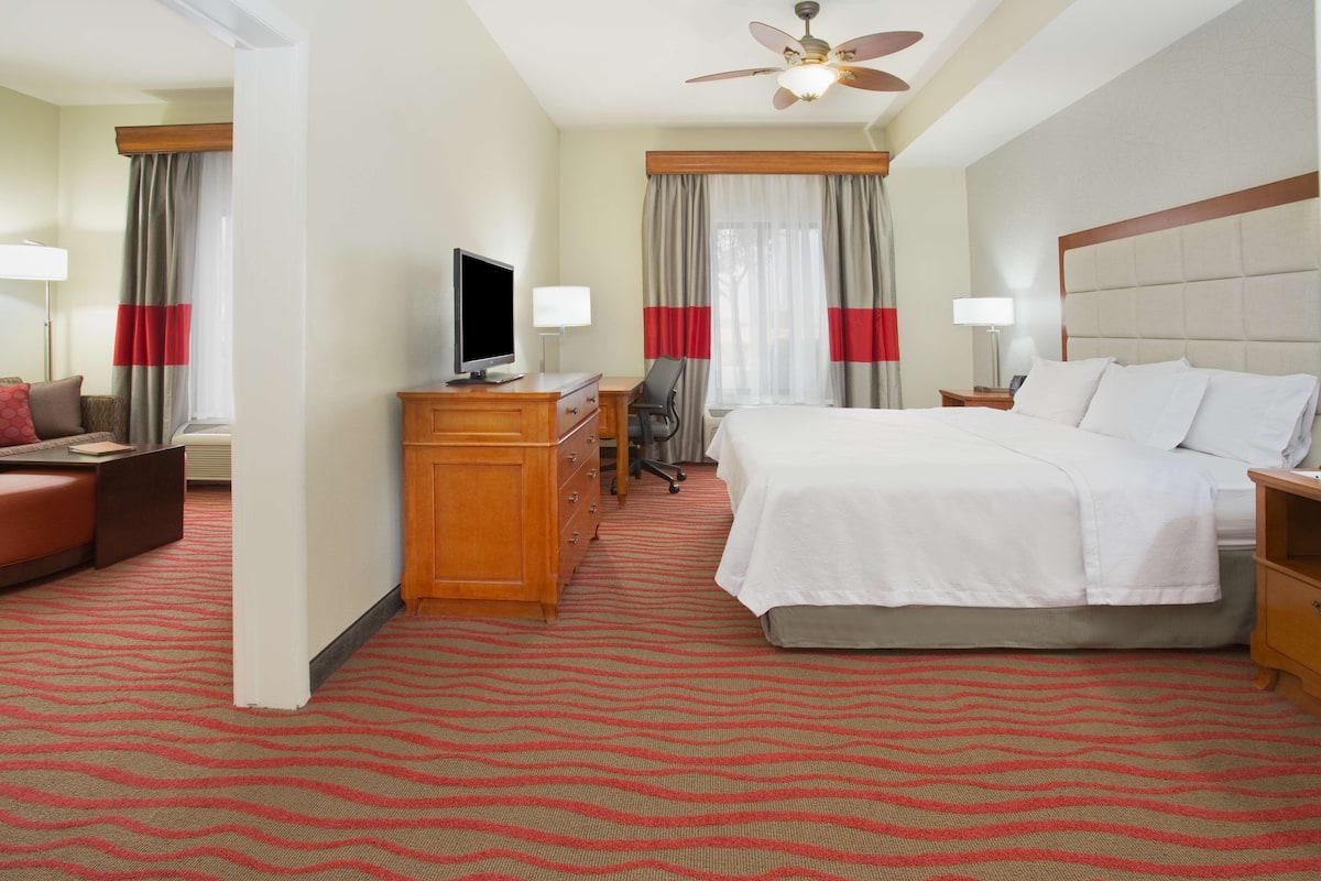 A hotel room with a bed, a desk with a computer, a chair, a TV, and a lamp.