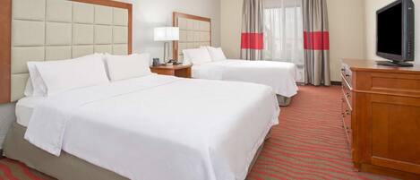 A hotel room with two beds, a television, a desk, and a window with curtains.