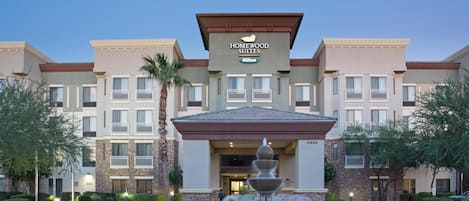 A hotel entrance with a fountain, multiple balconies, and a clear sky.