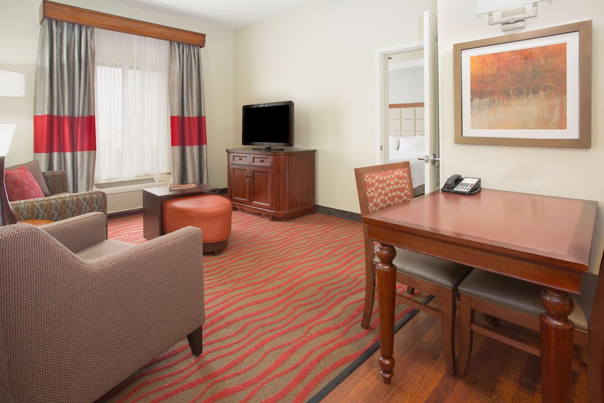 A hotel room with a sofa, a dining table, a television, and a painting on the wall.