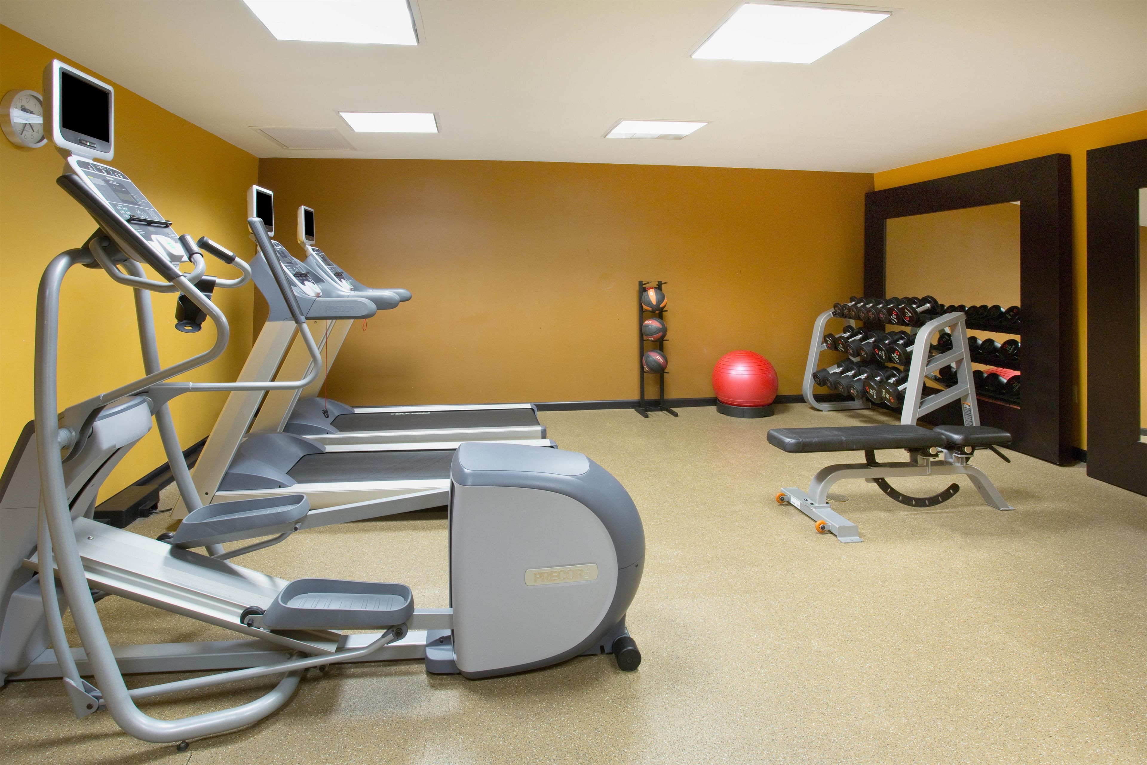 Una palestra con tapis roulant, cyclette, una palla rossa per esercizi e un porta pesi.