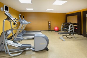 A gym with treadmills, a stationary bike, a red exercise ball, and a rack of dumbbells.