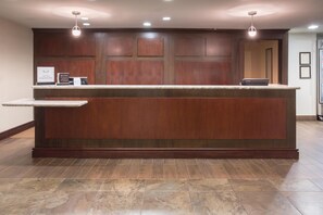 A hotel reception area with a marble counter, wooden paneling, and a modern light fixture.