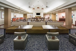 A hotel lobby with a seating area, a television screen, and a reception desk.