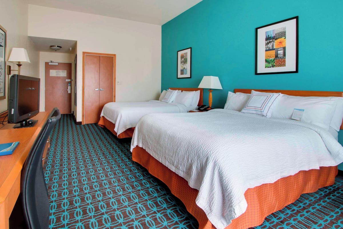 A hotel room with two beds, a desk with a computer, and a TV.