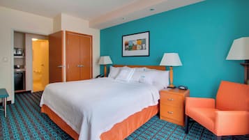 Quarto de hotel com uma cama grande, duas mesas de cabeceira com luminárias, um guarda-roupa de madeira, uma mesinha e uma poltrona laranja.