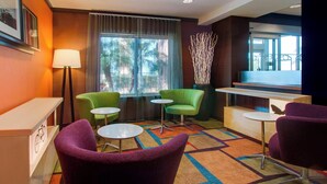 A hotel lobby with a reception desk, green and purple chairs, small tables, a colorful carpet, and a large window with a view of palm trees. - Fairfield Inn & Suites by Marriott Clermont (Clermont)
