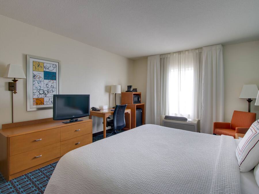A hotel room with a large bed, a desk, a chair, a television, and a painting on the wall.