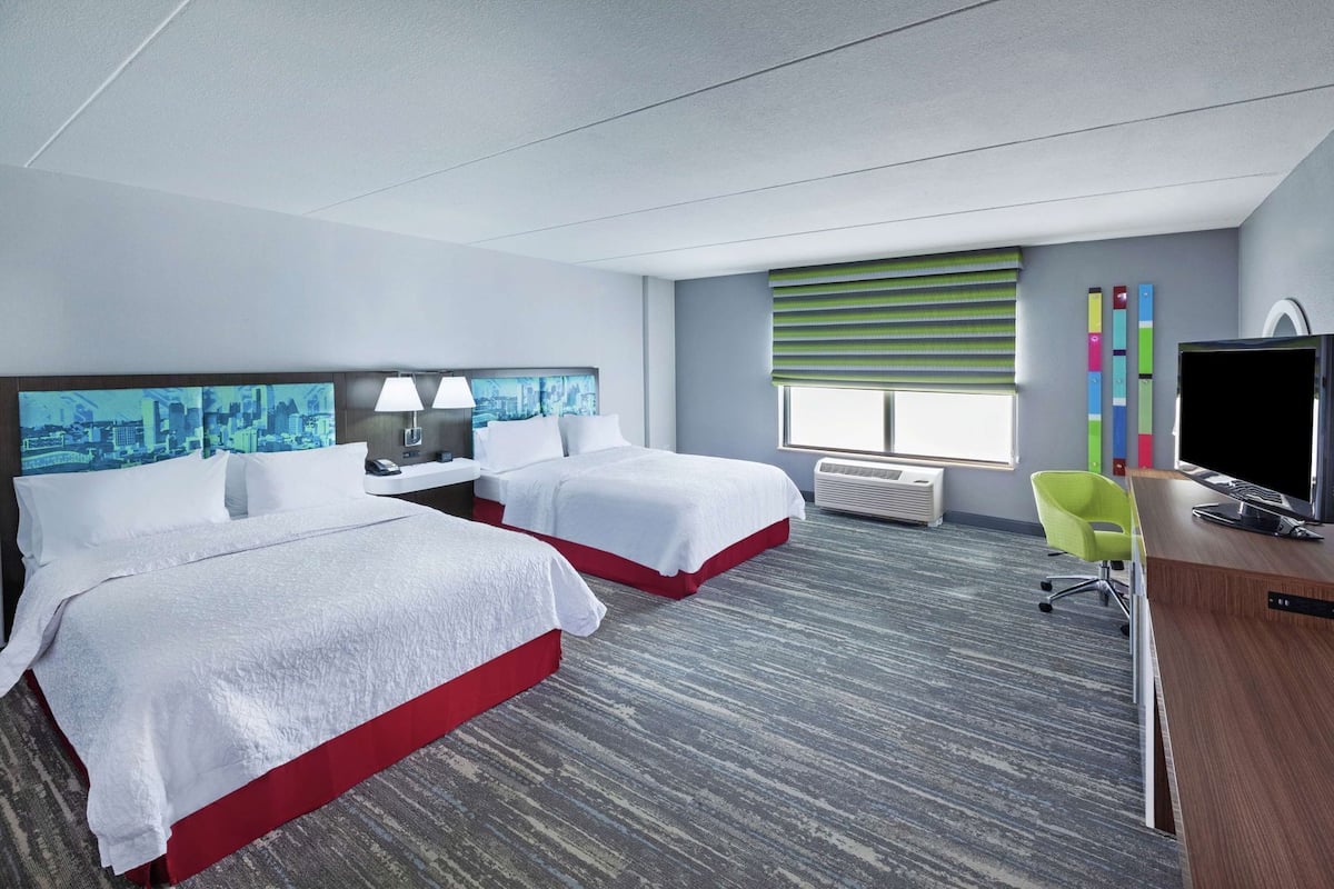 A hotel room with two beds, a desk with a TV, a chair, and a window with blinds.