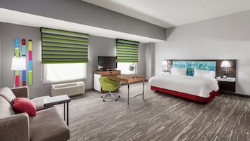 A hotel room with a bed, desk, chair, TV, and air conditioning unit.