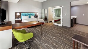 A modern hotel room with a large bed, a desk, a green chair, a mirror, and a bathroom visible through an open door. - Hampton Inn & Suites Houston-Bush Intercontinental Aprt (Houston)
