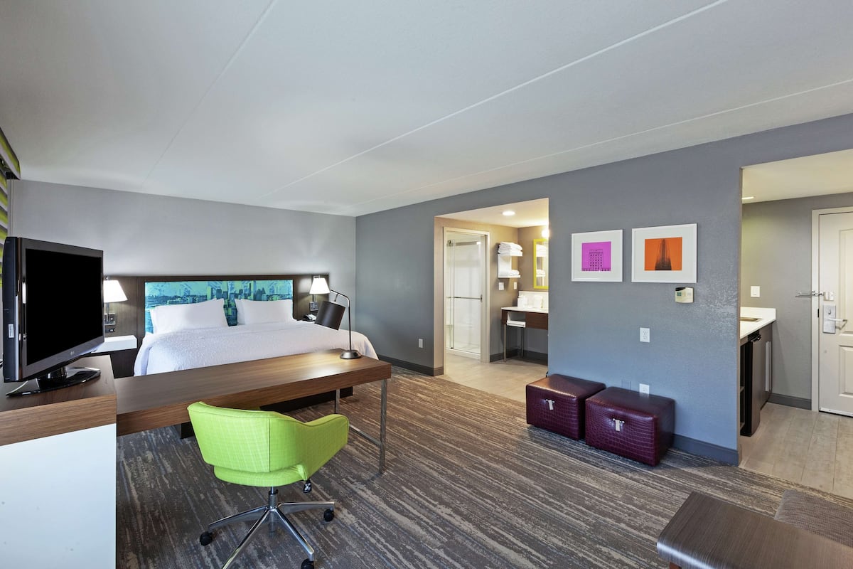 A hotel room with a bed, desk, green chair, and a TV.