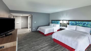 A hotel room with two beds, a television, a desk, and a cityscape painting on the wall.