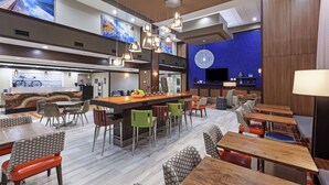 A modern hotel lobby with a bar area, seating arrangements, and a large screen displaying cityscapes. - Hampton Inn & Suites Houston-Bush Intercontinental Aprt (Houston)