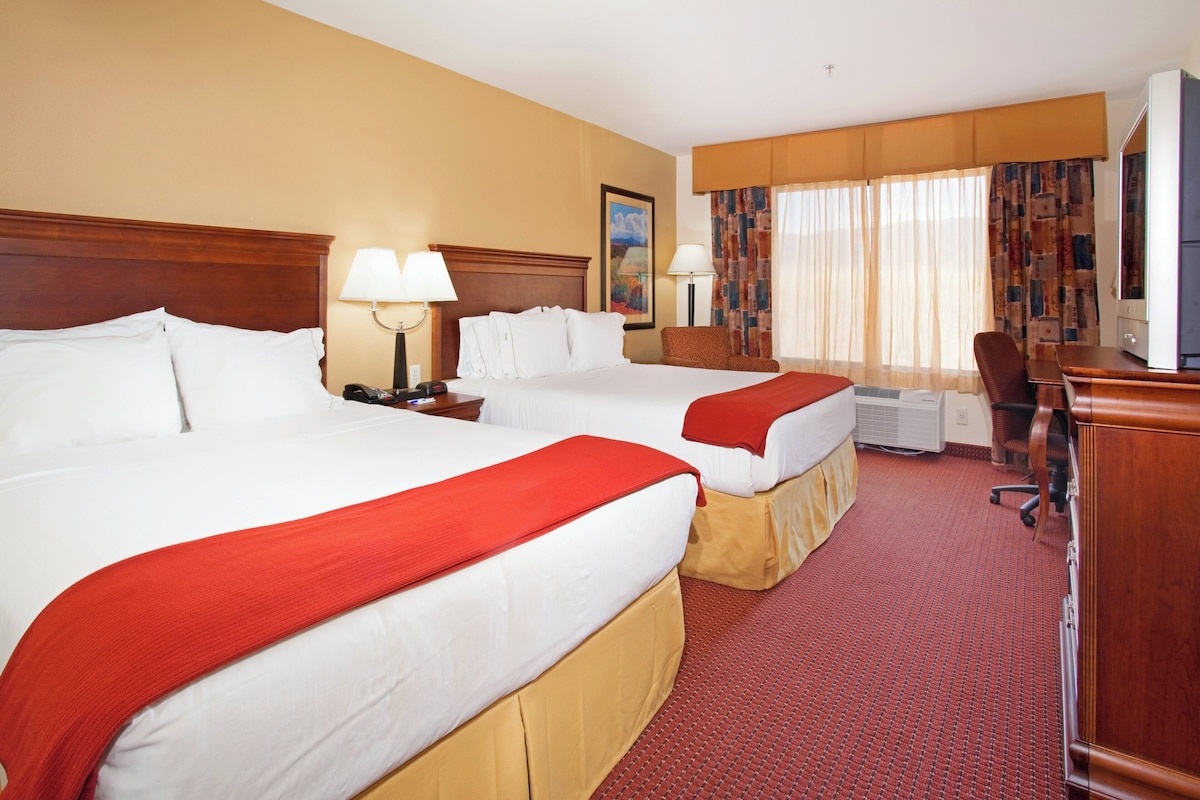 A hotel room with two beds, a desk, a chair, and a television.