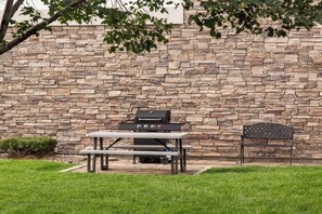 A stone wall with a barbecue grill and a table and chair set in front. - Holiday Inn Express & Suites Tooele by IHG (Tooele)
