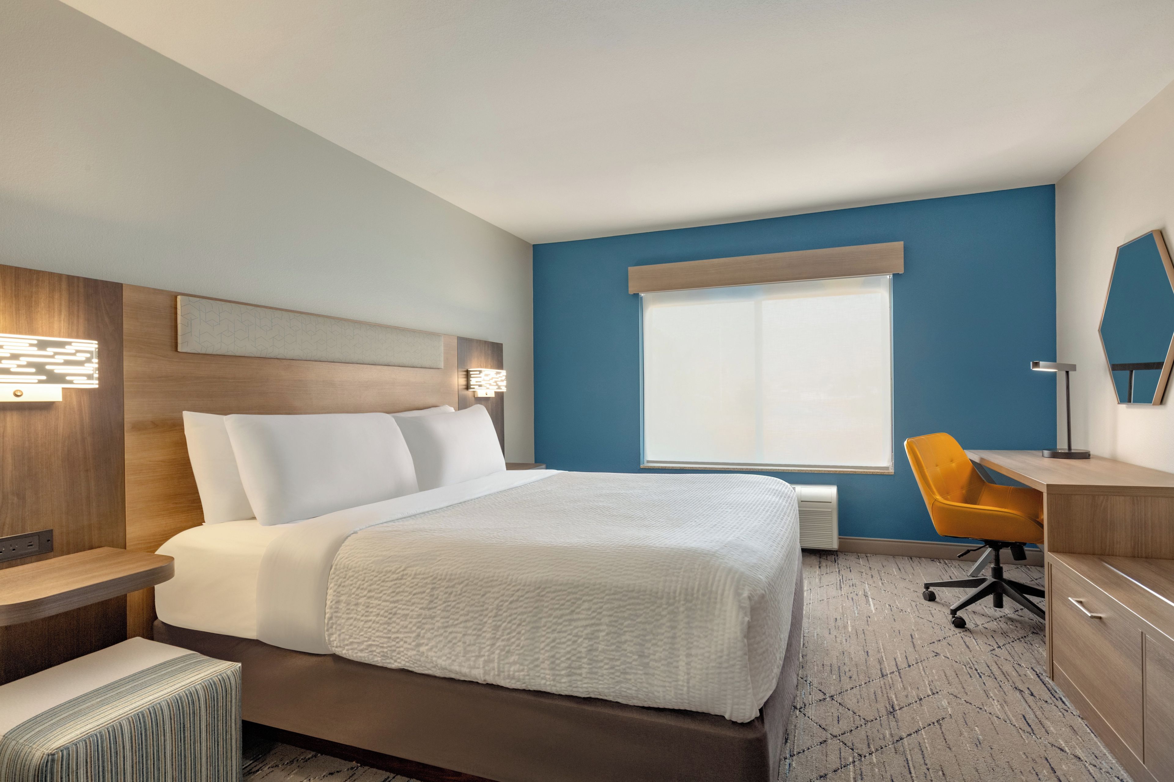 A hotel room with a bed, a desk, a chair, and a window.