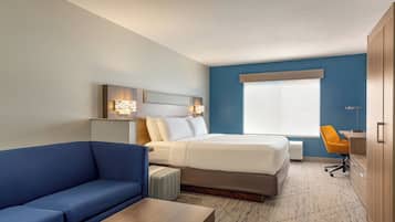 Una habitación de hotel con una cama, un sofá azul, un escritorio y una ventana con persianas.