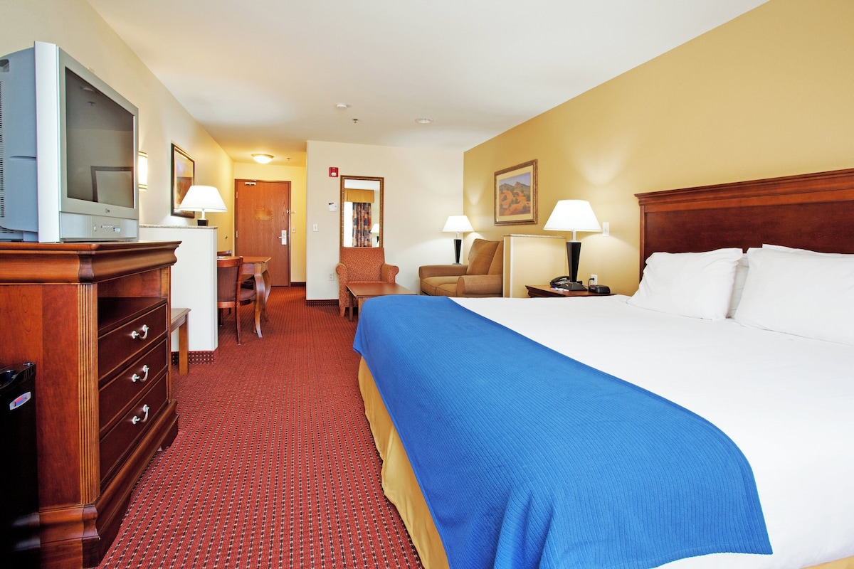 A hotel room with a large bed, a desk, a chair, a television, and a wardrobe.