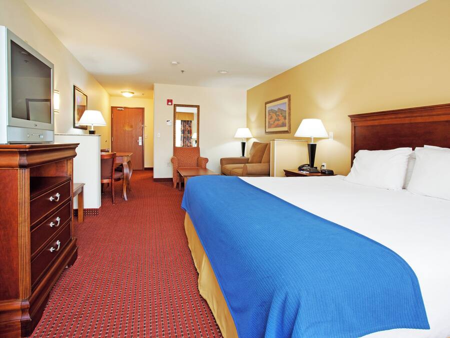 Una habitación de hotel con una cama grande, un escritorio, una silla, un televisor y un armario.