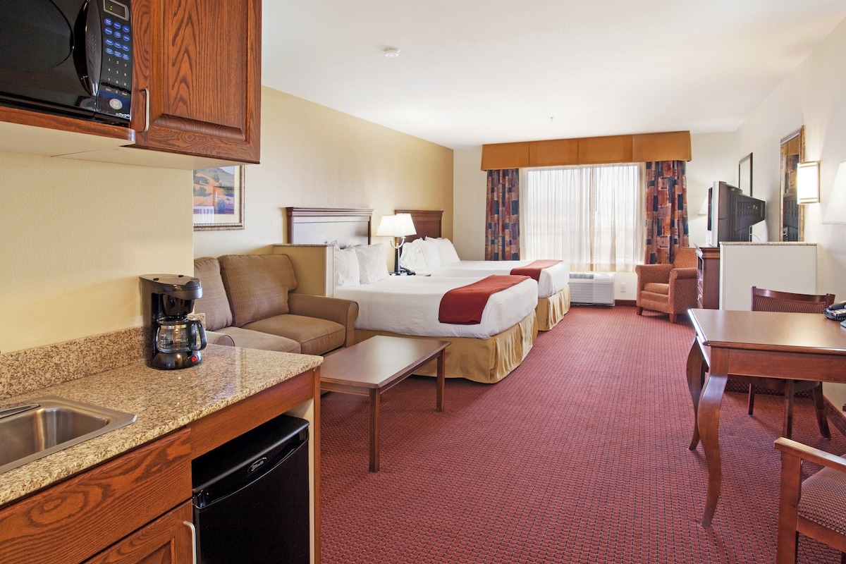 A hotel room with a kitchenette, a bed, a sofa, a dining table, and a television.